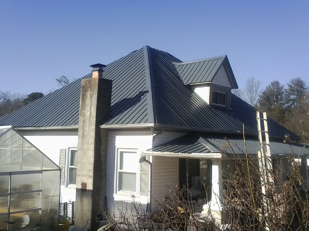 Dark blue standing seam metal roof on a white farmhouse with dormer — Slate & Tile Roof Repair by Roofing Brothers in Byron