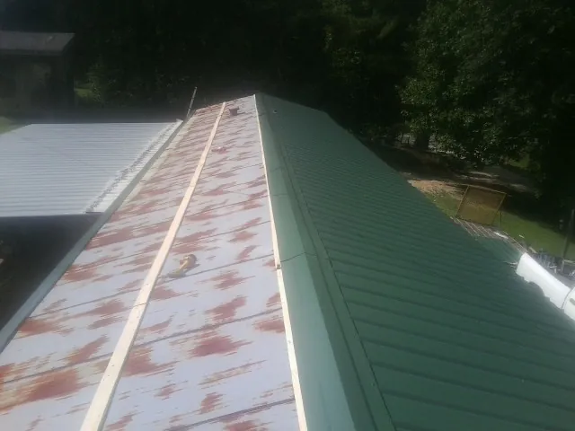 Old rusted panels beside newly installed green metal roofing — Wind Damage Roof Repair by Roofing Brothers in Byron